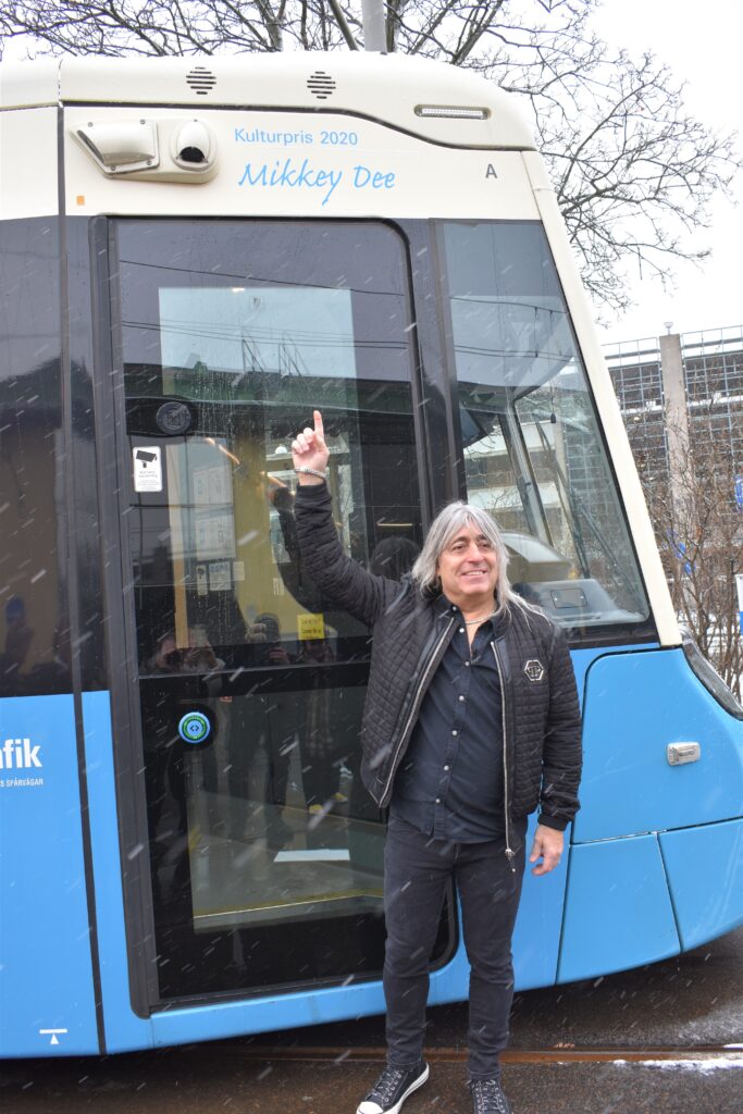 Mikkey Dee står vid en spårvagn och pekar på den