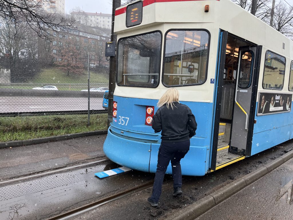 En blond, mörkklädd kvinna bakom en stillastående spårvagn som står över en poängbräda.